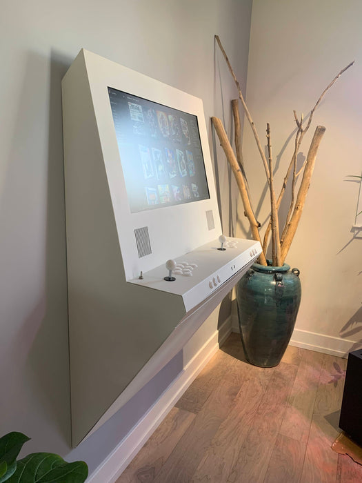 Wall-mounted electronic device with digital display next to a vase with sticks on a wooden floor.