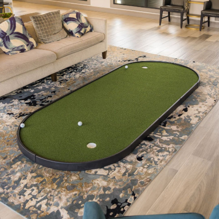 Green putting green mat with golf balls on a patterned rug in a living room.