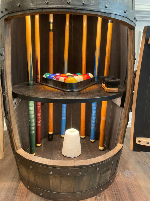 Pool cue rack inside a wooden barrel with pool balls and a triangle.