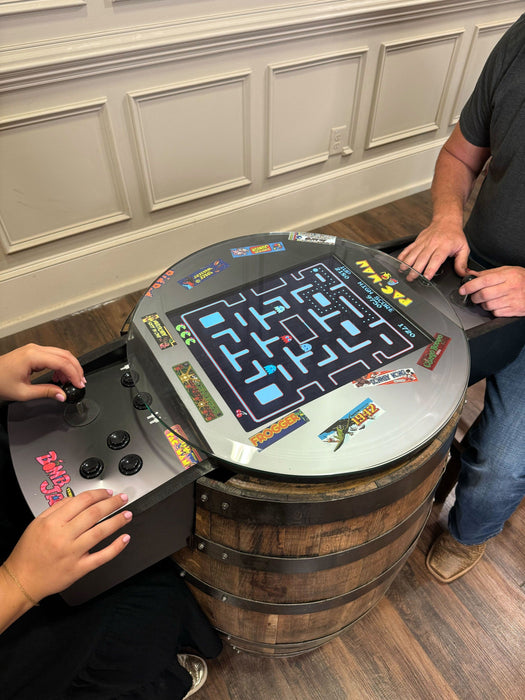 Two people playing a Pac-Man arcade game on a barrel table.