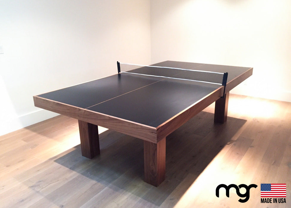 Wooden ping pong table with black surface on a wooden floor, MG brand visible.