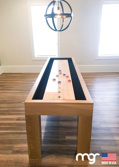 Wooden shuffleboard table with balls on a wooden floor in a room with large windows.