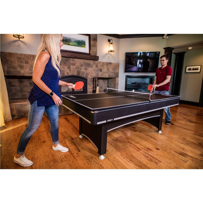 Two people playing ping pong in a living room with a fireplace and television.