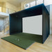 Black and green Golf Simulator booth setup in a room with stairs and large windows.