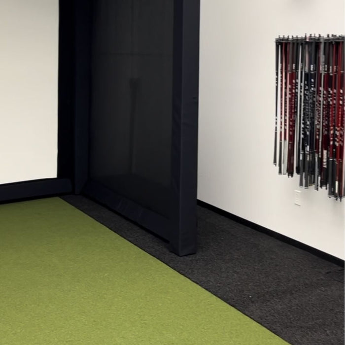 Green carpeted floor corner with a black wall and a white wall with hanging items.