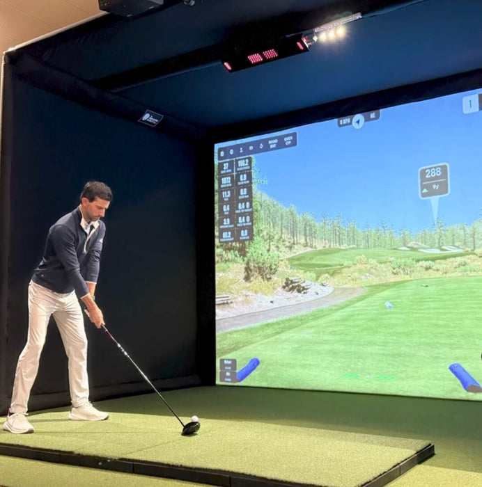 Man playing golf in a simulator with a screen displaying a golf course.