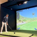 Man playing golf in a simulator with a screen displaying a golf course.