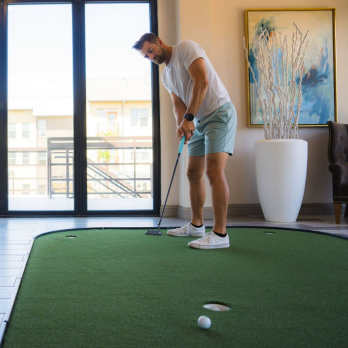 Man practicing golf indoors on a green mat with a modern interior background