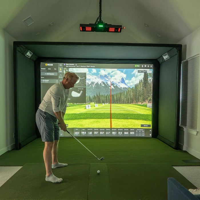 Man playing golf in a virtual reality simulator with a large screen displaying a golf course.