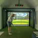 Man playing golf in a virtual reality simulator with a large screen displaying a golf course.