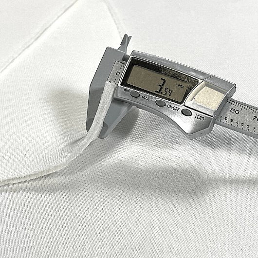 Digital caliper measuring a white fabric with a digital display showing a measurement.