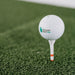 Golf ball on a tee with 'Indoor Golf Shop' branding on a green grass background