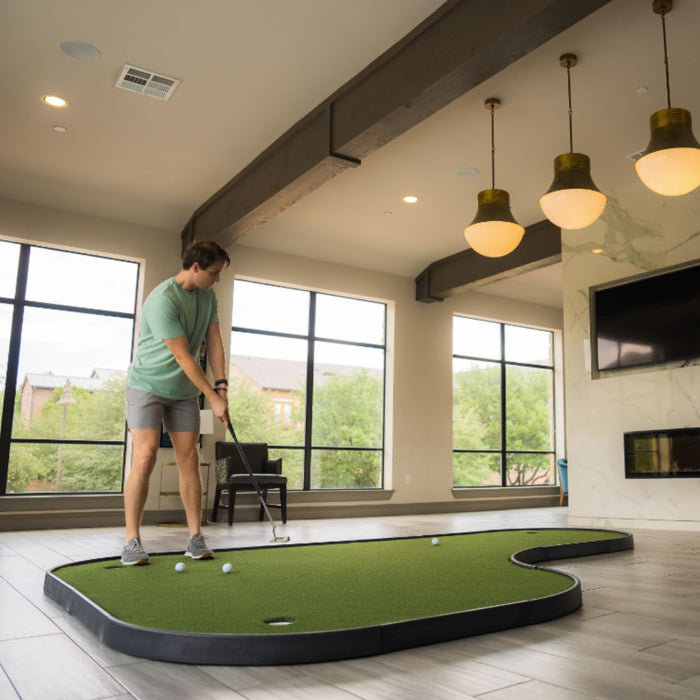 Person playing indoor putting green in a modern room with large windows.