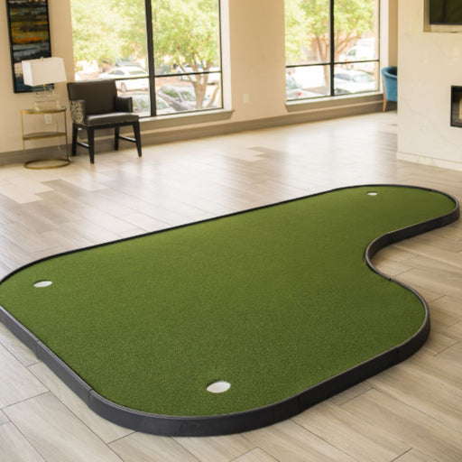 Green indoor putting green mat on a wooden floor with large windows in the background.